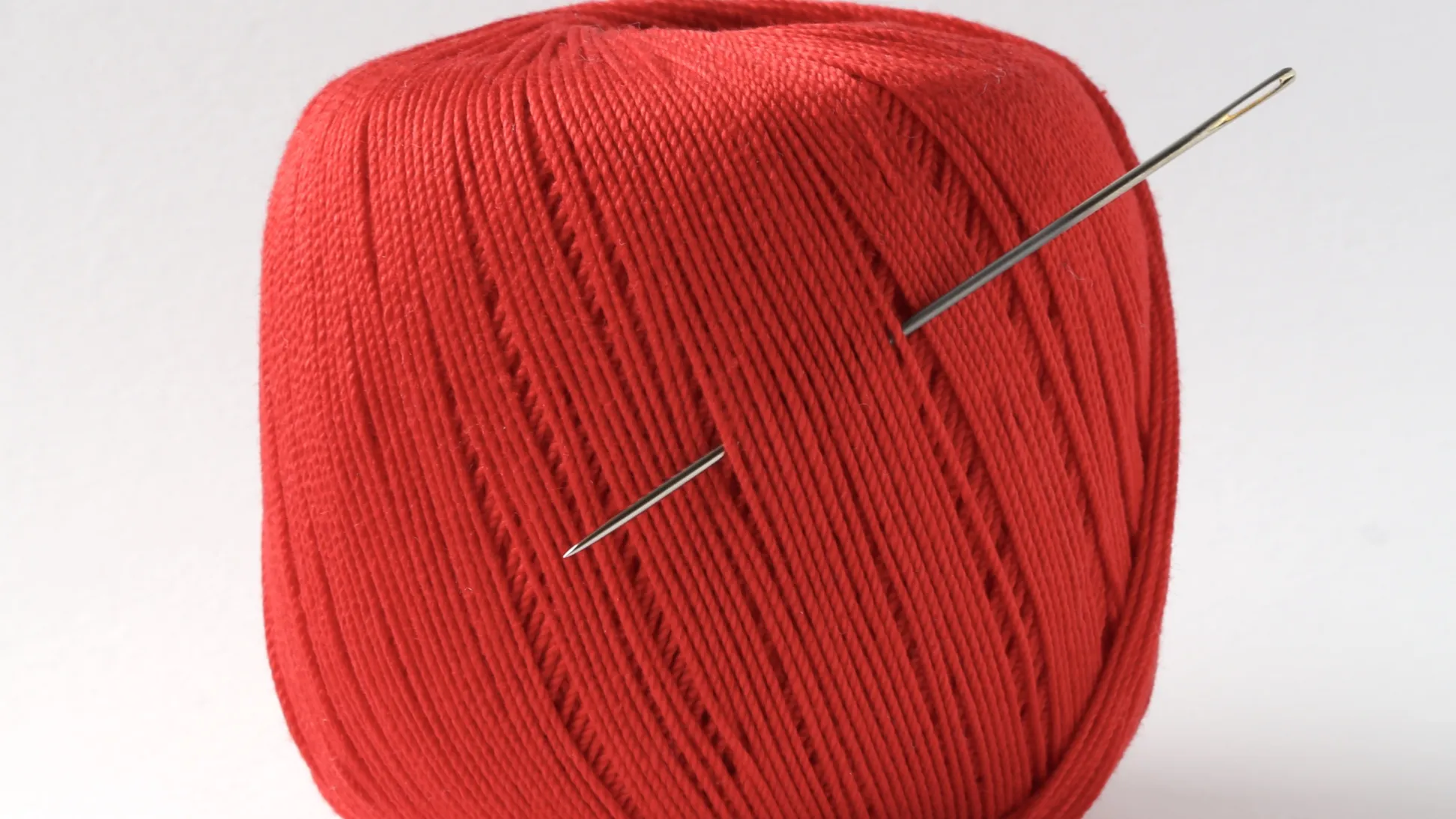 A roll of darning thread in red with a needle poked into the front
