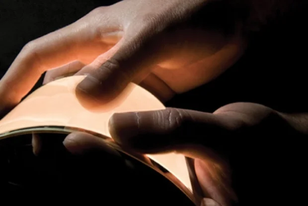 a close up of hands bending a flexible sheet that omits a glowing orange light