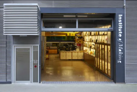 An exterior view of a building with large front doors opened up to reveal the interior Materilas Library and workshop. On the right hand side of the door frame a log reads "Institute of Making"