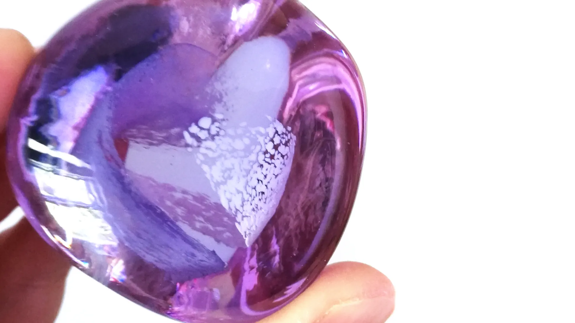 A close up of a pebble of glass held between finger tips that changes colour under different light sources. It currently looks a light purple